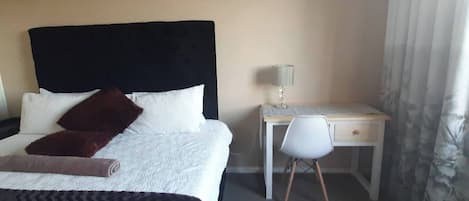 A hotel room with a bed, a desk, a chair, and a lamp.