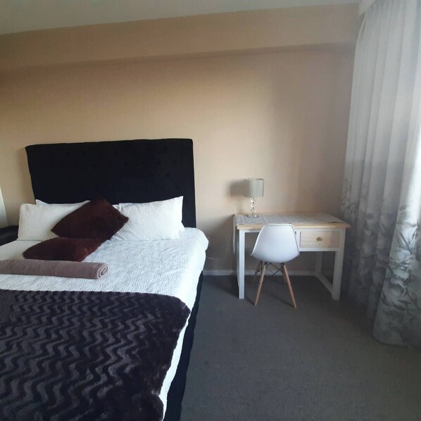 A hotel room with a bed, a desk, a chair, and a lamp.