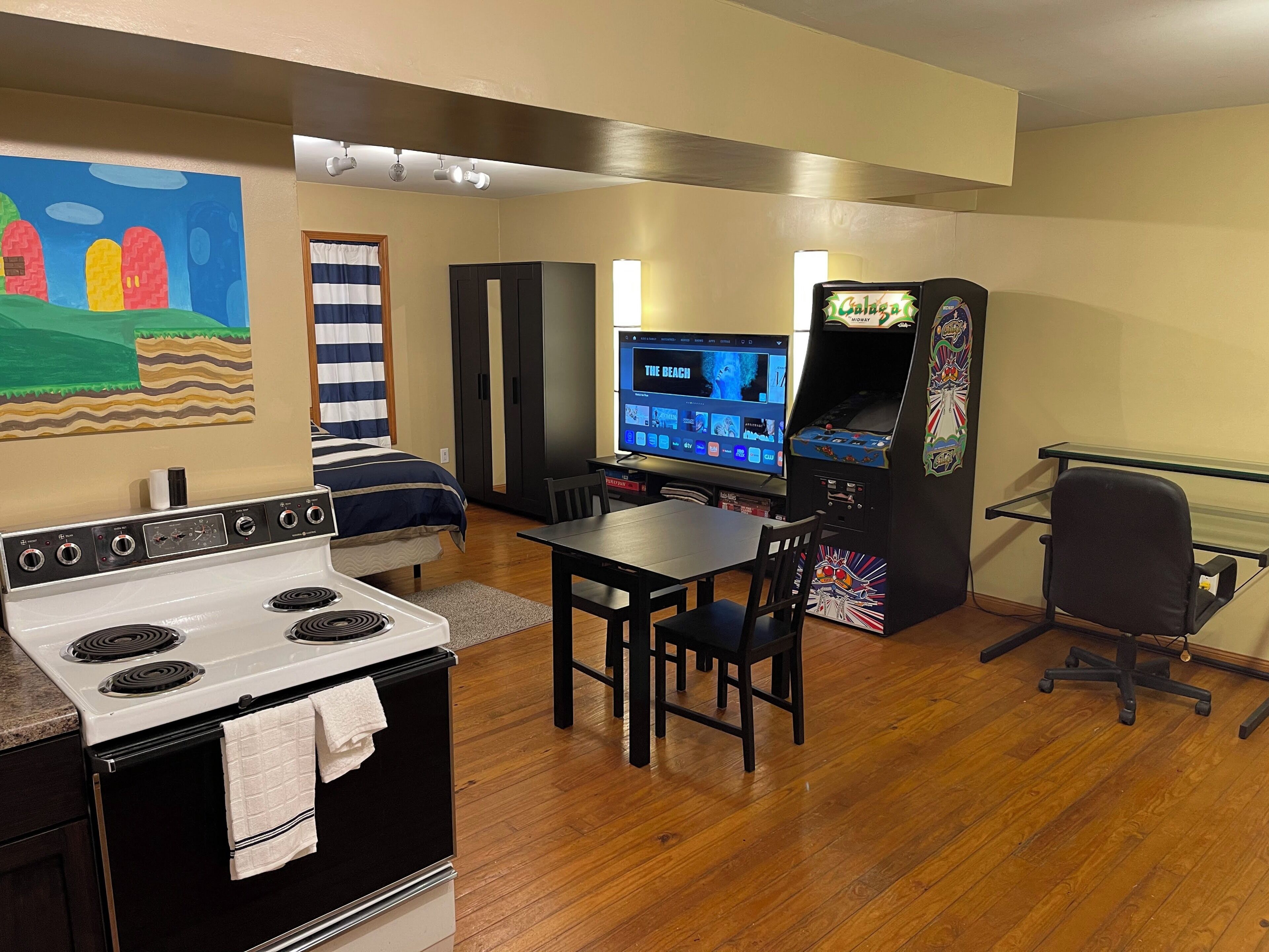 Une cuisine équipée d’une cuisinière, une table à manger avec des chaises, un téléviseur et une console de jeux vidéo.
