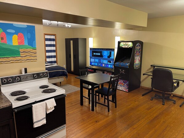 A kitchen with a stove, a dining table with chairs, a TV, and a video game console.