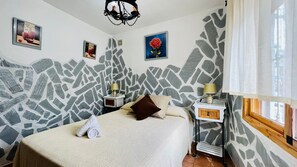 Ein Schlafzimmer mit einer Wand im Steinmuster, einem Bett mit gerolltem Handtuch, zwei Nachttischen mit Lampen und Bildern an den Wänden.