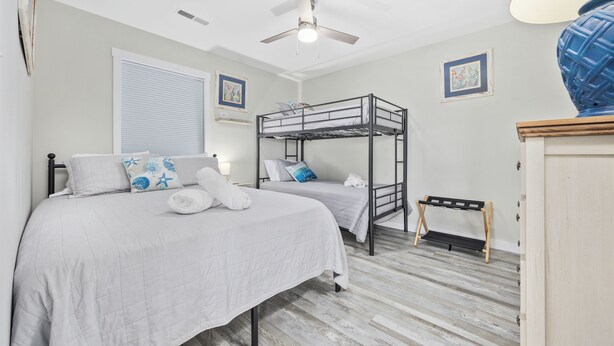 A bedroom with two beds, a ceiling fan, a window with blinds, and a small table. - Updated Condo with pool within walking distance to beach (North Myrtle Beach)