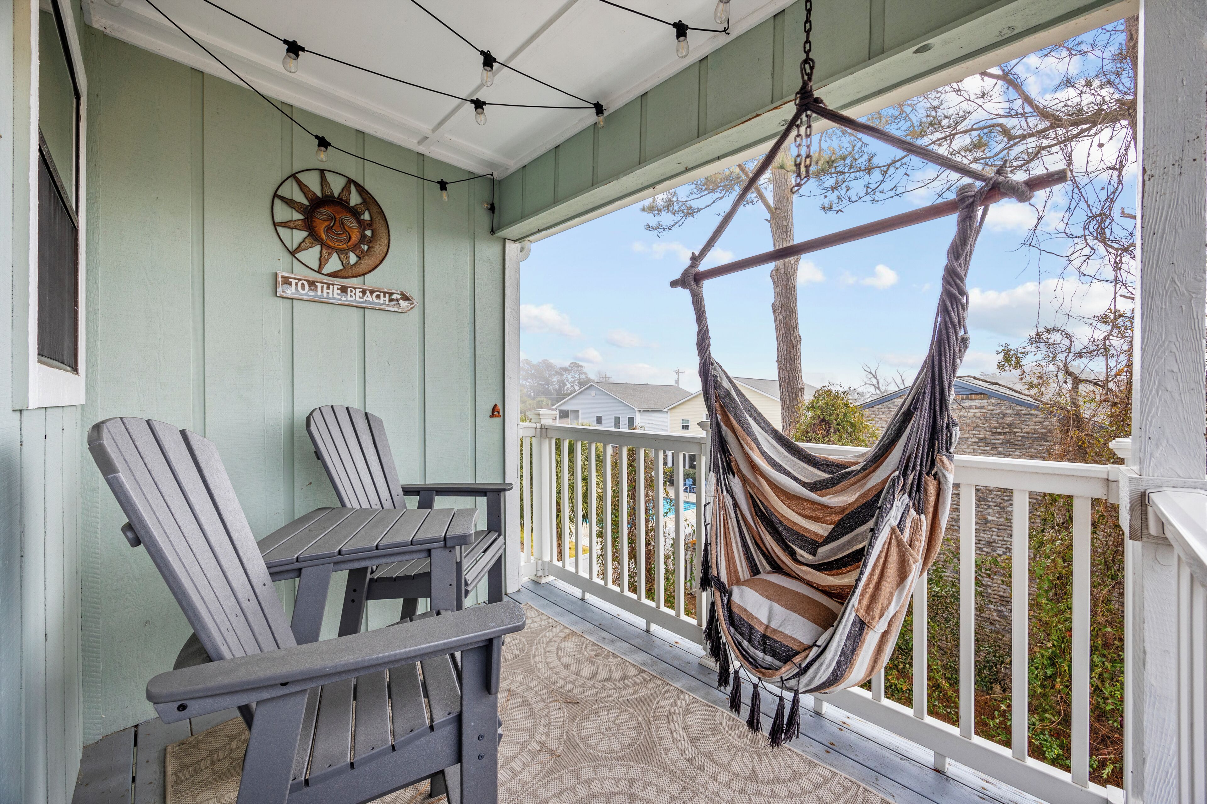 A porch with Adirondack chairs, a hammock, and a sign reading 'TO THE BEACH'.