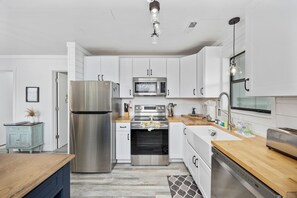 A modern kitchen with stainless steel appliances, white cabinetry, and a wooden countertop. - Updated Condo with pool within walking distance to beach (North Myrtle Beach)