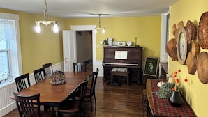 Un coin repas avec une table et des chaises en bois, un piano et des décorations murales en osier.