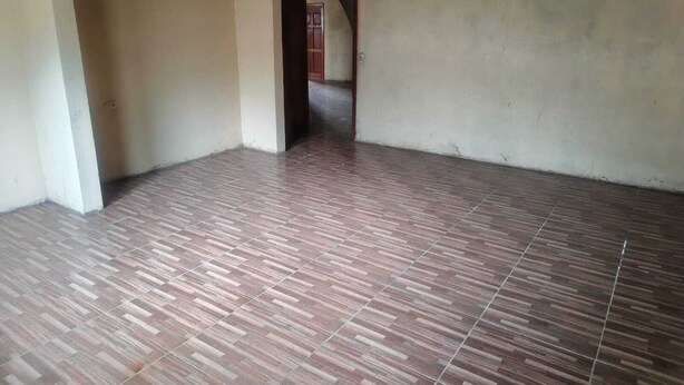 Una stanza con pavimento piastrellato, una porta che dà su un'altra stanza e pareti spoglie.
