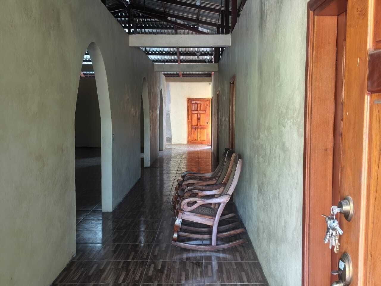 A hallway with wooden rocking chairs lined up against the wall, leading to a wooden door with a key in the lock.