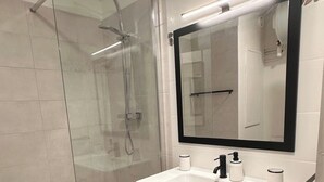 Une salle de bain moderne avec une douche à parois de verre, un meuble-lavabo en bois avec un miroir et un lavabo blanc.