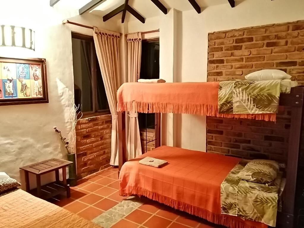 Ein Zimmer mit einem Etagenbett, einem kleinen Tisch, einem Fenster mit Vorhängen und einer Backsteinwand.
