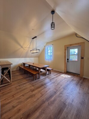 Ein Zimmer mit einem Holztisch, Bänken, einer Tür mit Fenster und einer Deckenleuchte.