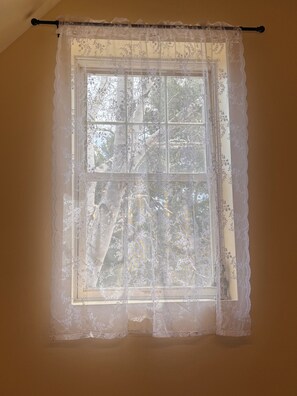 Ein Fenster mit Spitzenvorhang, Holzrahmen und Blick auf Bäume.