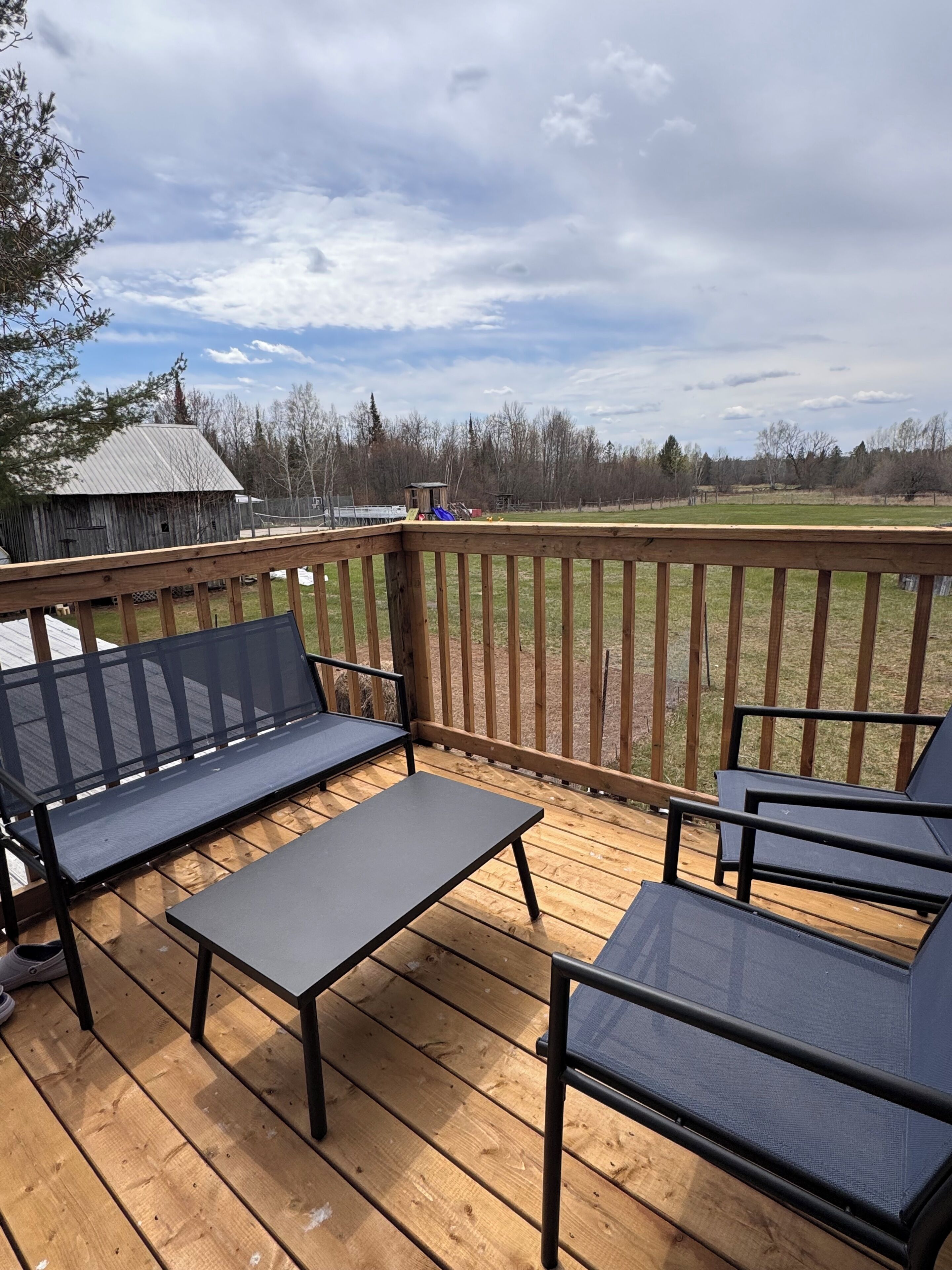 A wooden deck with outdoor furniture, a view of a fenced yard, and a building in the background.