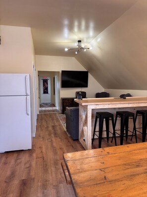 A modern kitchen with a wooden island, black bar stools, a flat-screen TV, and a refrigerator. - The Loft at New Frontiers Retreat, group/large family lodge in country setting . (North Algona Wilberforce)