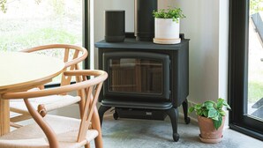 Ein Zimmer mit einem Holztisch, Stühlen, einem schwarzen Kaminofen und einer Blumentopf-Pflanze.