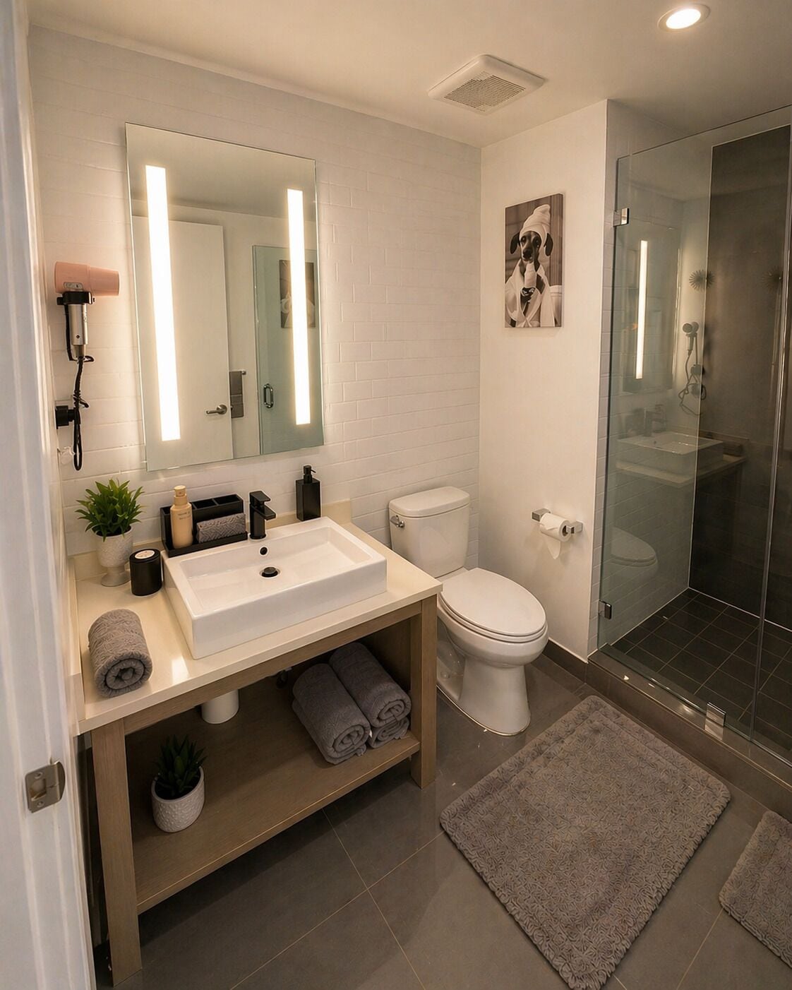 Un baño moderno con un espejo grande, lavamanos blanco, inodoro y cabina de ducha de vidrio.