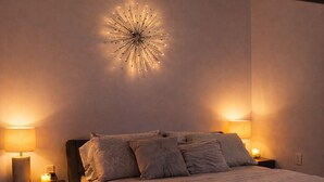 Une chambre à coucher moderne avec un lit, deux lampes de chevet, un luminaire fixé au mur et une table de chevet.