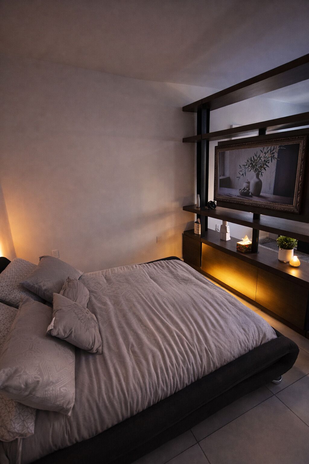 Een moderne slaapkamer met een bed, nachtkastjes, een wandplank met decoratieve objecten en een ingelijst schilderij.