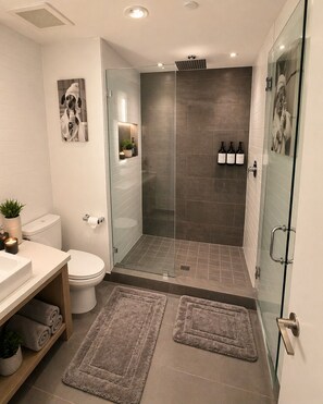 Un baño moderno con inodoro, lavabo, cabina de ducha de vidrio y dos alfombras.