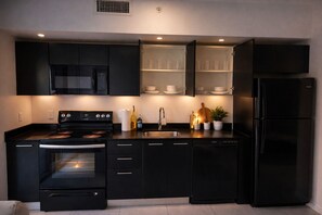 Eine moderne Küche mit schwarzen Schränken, einem Backofen, einer Mikrowelle, einem Kühlschrank und einem Glastrennschrank mit Tassen und Schüsseln.