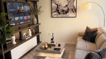 A modern living room with a flat-screen TV, a sofa, a coffee table, and a painting on the wall.