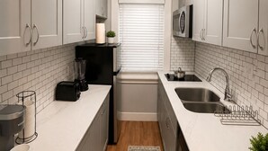 Een moderne keuken met witte kastjes, een zwarte koelkast, een inbouwoven, een magnetron en een spoelbak.