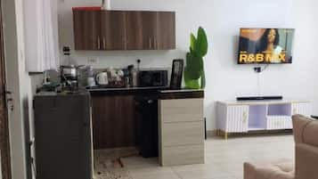 Une cuisine moderne équipée d’un réfrigérateur, d’un four à micro-ondes et de placards. On y trouve également un coin repas avec un canapé et un téléviseur diffusant « R&B NIX ».