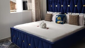 A bedroom with a large bed, a window with curtains, a wall-mounted artwork, and a ceiling light. - SPACIOUS VIP 1 BEDROOM with ROOFTOP SWIMMING POOL AVAILABLE (Mtwapa)