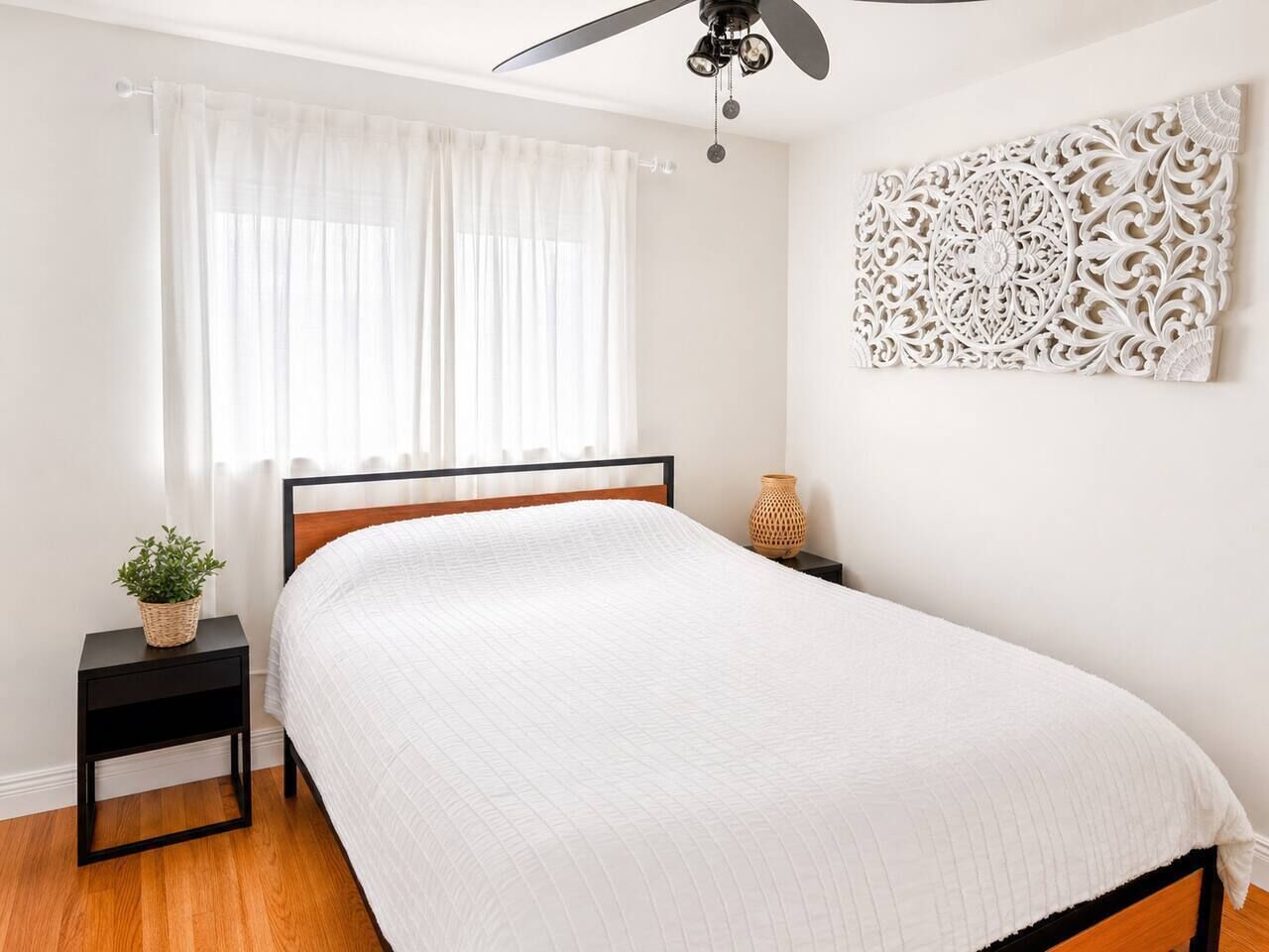 Une chambre à coucher comprenant un lit, une table de chevet, un élément décoratif fixé au mur et un ventilateur de plafond.