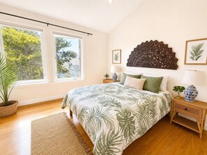 Un dormitorio con una cama grande, un cabecero decorativo en la pared, una planta en maceta y vistas a árboles a través de la ventana.