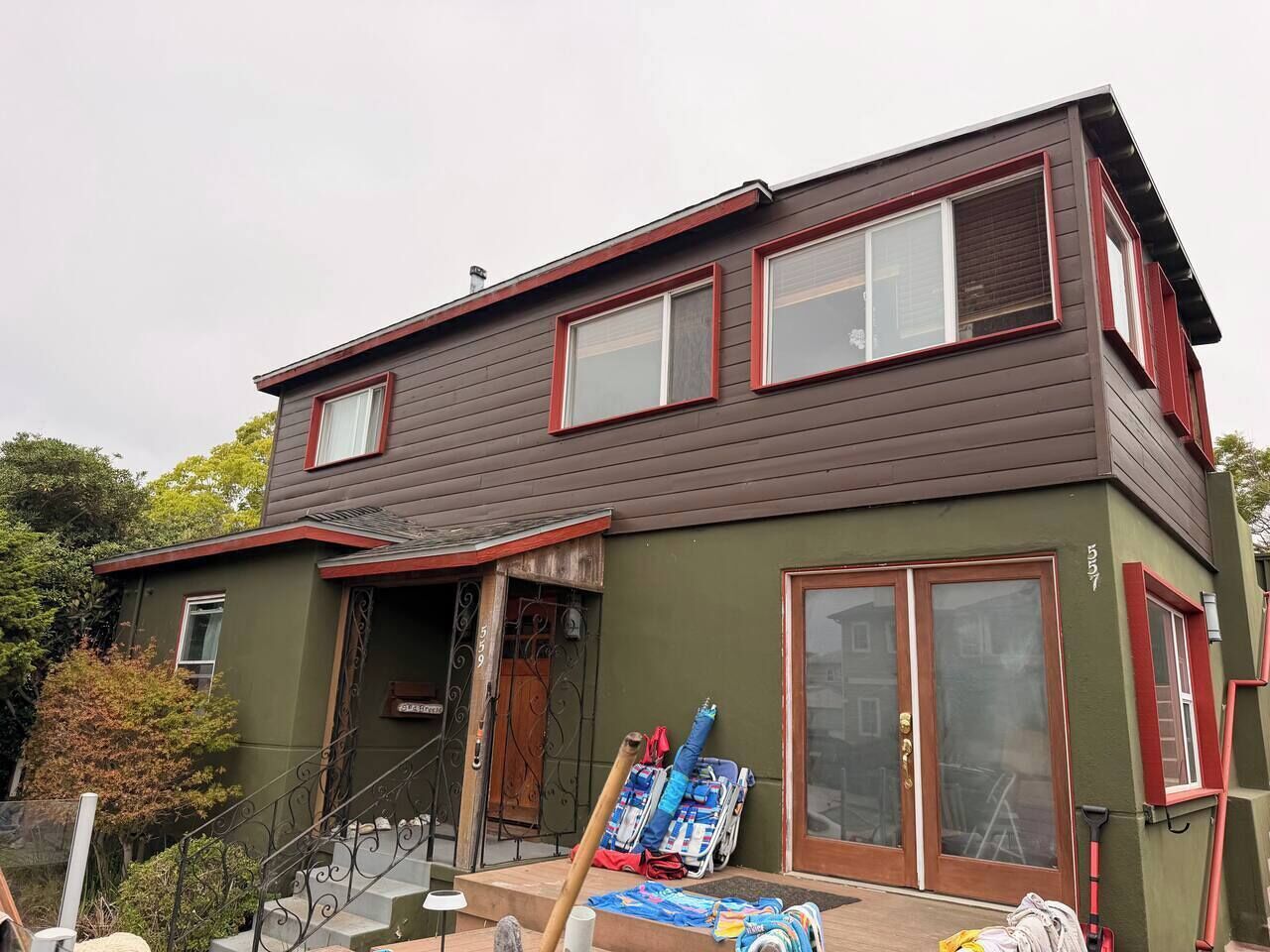 A two-story house with a brown exterior and red trim, a front porch, and a staircase leading to the entrance.