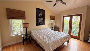 A bedroom with a bed, a ceiling fan, a window with blinds, a lamp, and a door leading to an outdoor area.