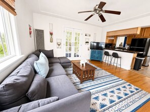 En moderne stue med en hjørnesofa, et sofabord og et køkkenområde med et køleskab og barstole.