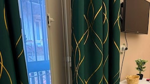 Una stanza con una porta scorrevole che dà su un balcone, una televisione fissata al muro e una piccola pianta in vaso su un tavolo.