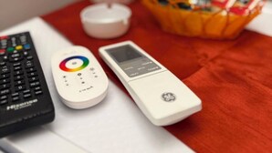 A remote control, a digital thermometer, and a smartphone on a table with a red cloth.