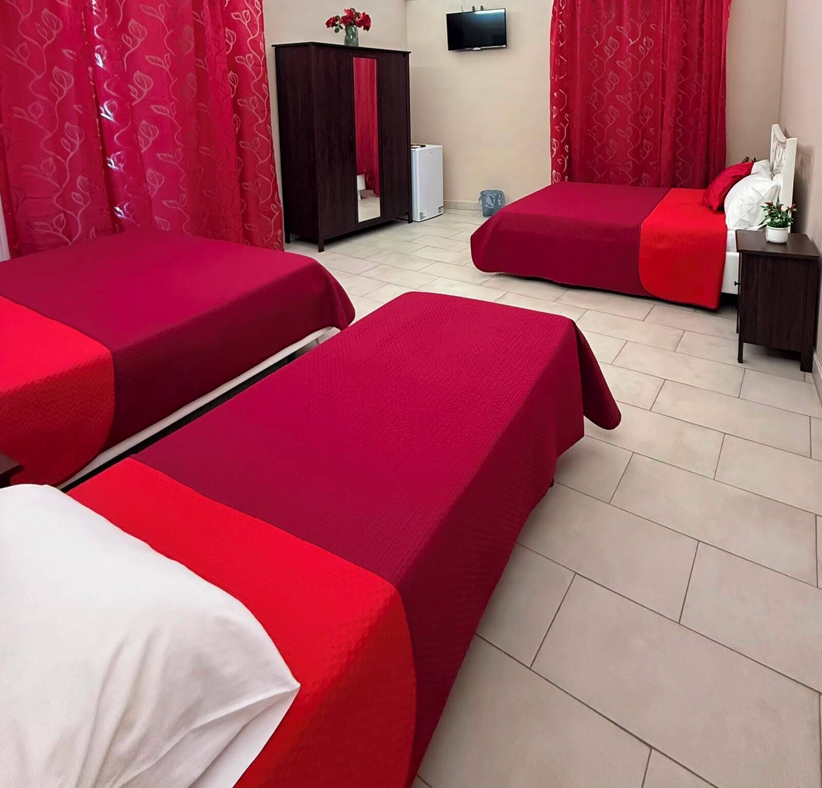 Ein Hotelzimmer mit zwei Betten, einem Fernseher, einem Kleiderschrank und einem kleinen Tisch mit Blumenvase.