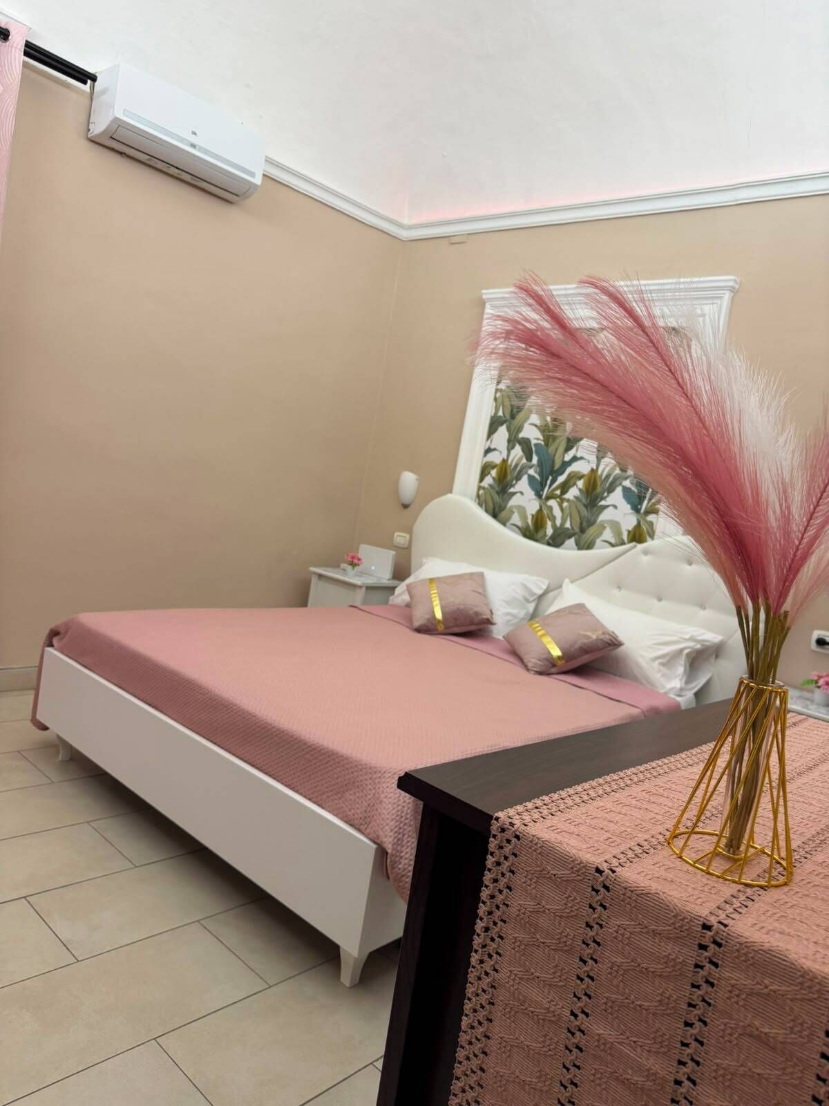 Un dormitorio con cama, mesita de noche, lámpara y planta decorativa.