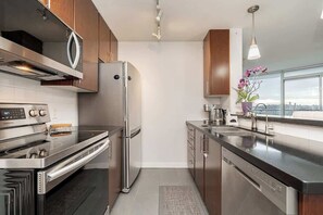 A modern kitchen with stainless steel appliances, wooden cabinets, and a view of the city. - Perfect Vancouver Getaway Central 2BR/2BA+Sofa Bed (Vancouver)