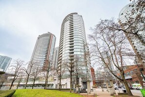 A modern building with a curved facade, surrounded by trees and a paved area with benches. - Perfect Vancouver Getaway Central 2BR/2BA+Sofa Bed (Vancouver)