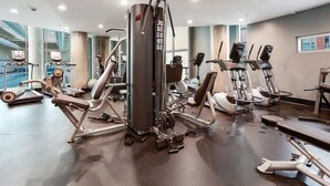 Un gimnasio con diversas máquinas de ejercicio, incluyendo una máquina central con varios agarres y una pila de pesas.