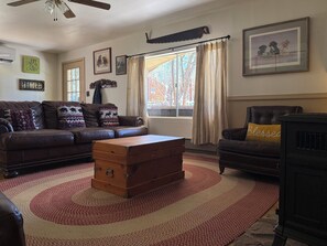 A living room with a brown leather sofa, a wooden chest, a black armchair, and a fireplace. - Serene 2-bedroom cabin with nestled in the pines. (Pine)