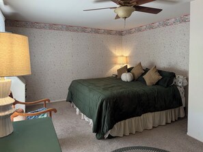 Una camera da letto con un letto, una ventola a soffitto, una lampada e una sedia.