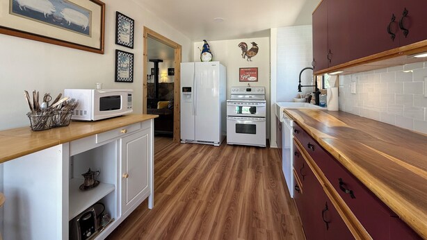 A compact kitchen with a microwave, refrigerator, oven, and wooden countertop. - Serene 2-bedroom cabin with nestled in the pines. (Pine)