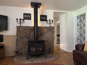 A stone fireplace with a black chimney, a television on the wall, and a brown leather sofa. - Serene 2-bedroom cabin with nestled in the pines. (Pine)
