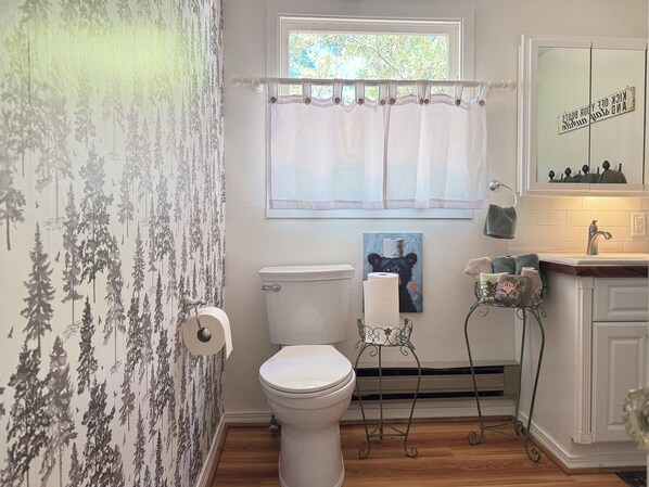Un bagno con il water, una finestra con tenda, un quadro di un orso e un lavandino con uno specchio.