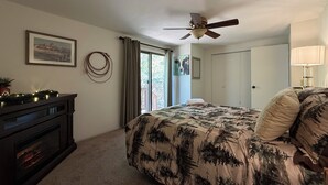A bedroom with a bed, a ceiling fan, a fireplace, a door, and a window. - Serene 2-bedroom cabin with nestled in the pines. (Pine)