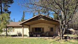 A single-story house with a covered patio area, a front door, and a small porch with seating. - Serene 2-bedroom cabin with nestled in the pines. (Pine)