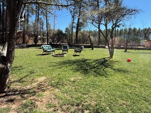 A grassy outdoor area with a wooden cabin, wicker chairs, and a red ball. - Serene 2-bedroom cabin with nestled in the pines. (Pine)