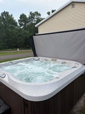 Ein Whirlpool mit Deckel, eine Holzterrasse und ein Haus im Hintergrund.