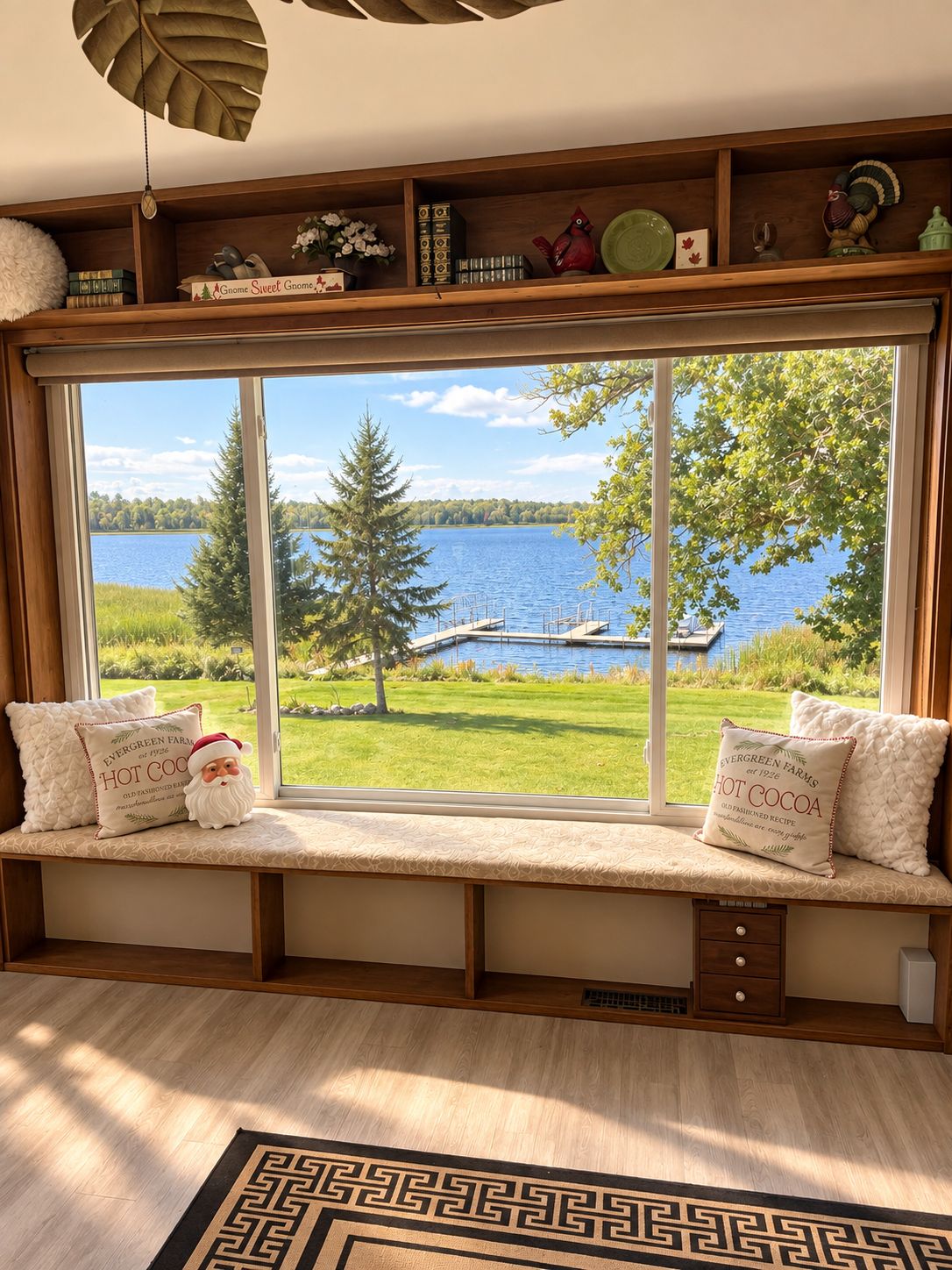 A room with a large window overlooking a lake, a wooden bench with decorative pillows, and a bookshelf with various items.