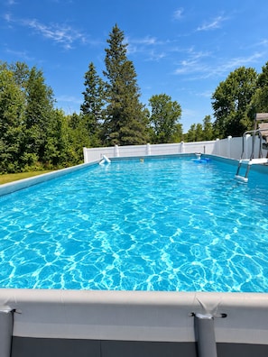 Ein klares, blaues Schwimmbecken, umgeben von einem weißen Zaun, mit Bäumen im Hintergrund.